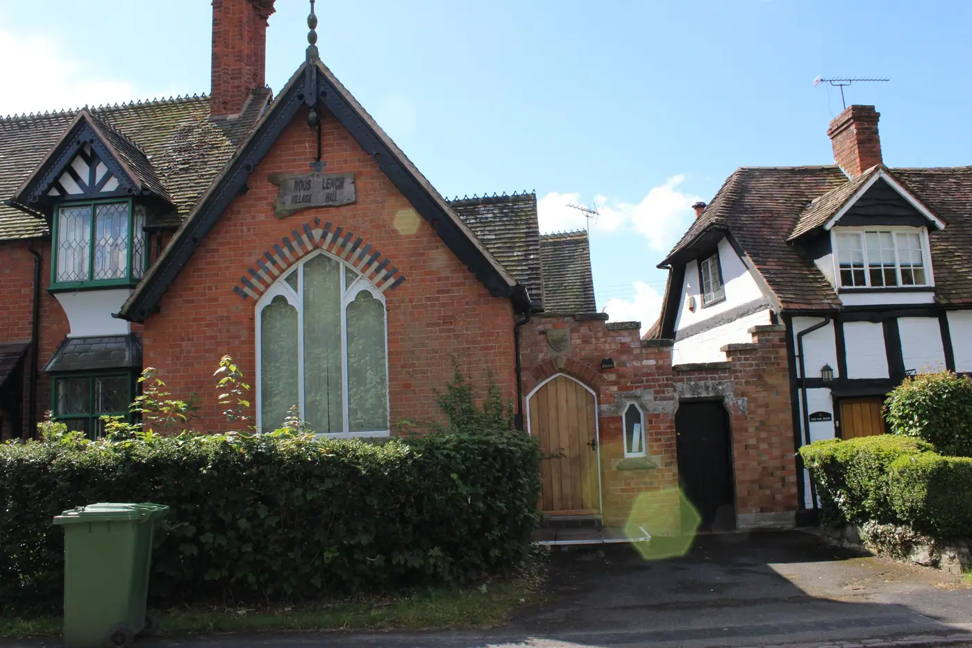 Rous Lench Village Hall, a red brick building with a gothic window and arched wooden doors, surrounded by hedges